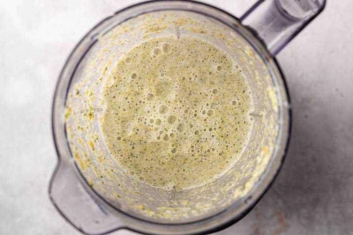 A blender filled with a foamy, light green mixture, viewed from above. The contents have a creamy texture, with small bubbles on the surface.